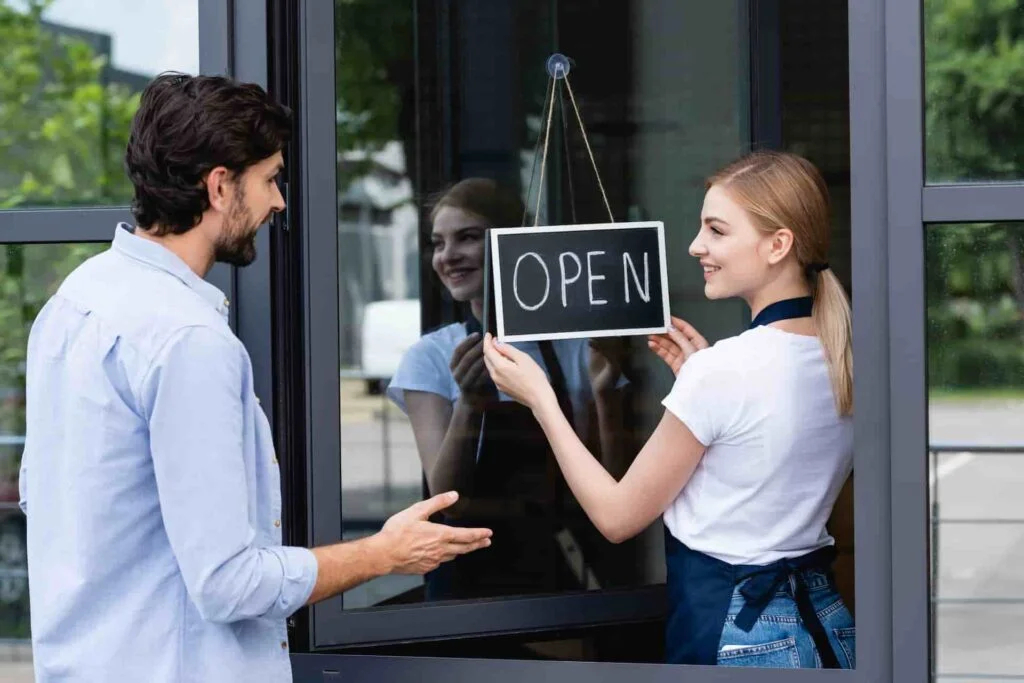 A local business owner discusses Web Design Payment Plan Options For Service Businesses while a woman places an Open sign on the door